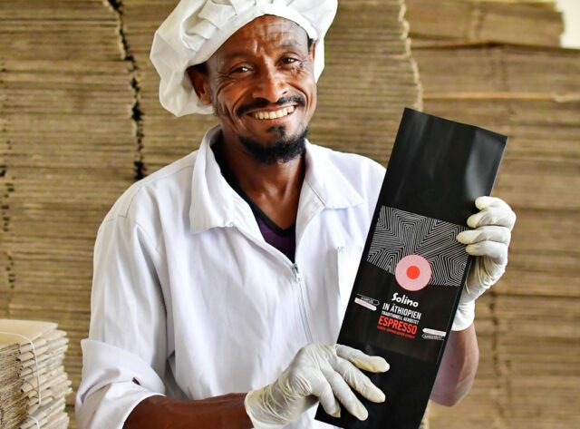 Äthiopischer Kaffeeproduzent hält lachend ein Päckchen Solino Coffee in die Kamera.