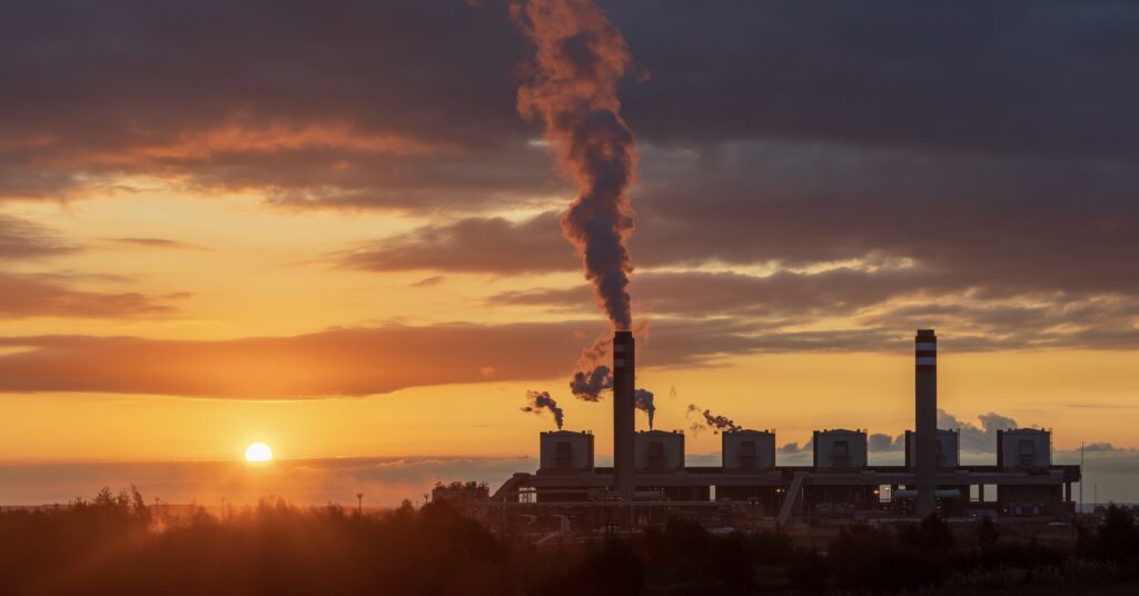 Image of factory with smoke with sunset in background.