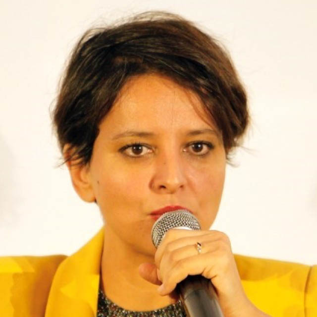 headshot of Najat Vallaud-Belkacem against a white background, holding microphone up against mouth