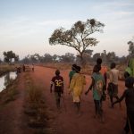 At the first light of day, Sudanese refugees walk towards a lake formed by floodwaters near the town of Yida, South Sudan. They are looking for mudfish. Late in the rainy season, children from Yida arrive by the hundreds to fish at the temporary lake. © Andrew McConnell